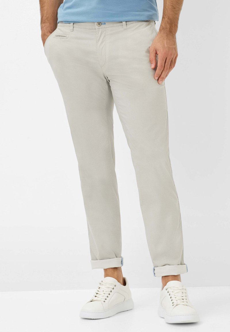 Chinos beiges clairs avec un motif texturé, coupe slim, et manches retroussées, associés à des baskets blanches avec bout rond et fermeture lacée.