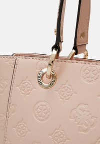 Poskipunan vaaleanpunainen keinonahkainen käsilaukku, jossa on kohokuvioidut kuviot ja kullanväriset metalliosat, mukaan lukien logorengas ja tummat hihnaosat.