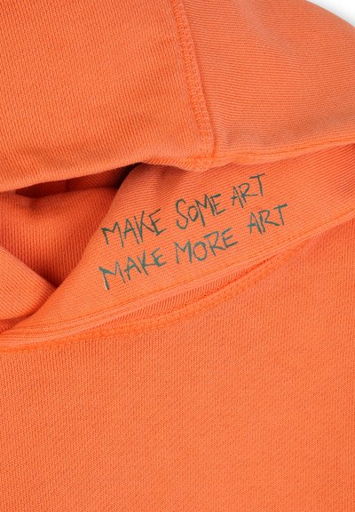 Sweat à capuche orange à texture côtelée, avec le texte « MAKE SOME ART MAKE MORE ART » brodé en vert à l'intérieur du col.