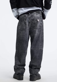 Pantaloni in denim grigio scuro con una vestibilità ampia, caratterizzati da un design a pannelli, doppi taschini posteriori e una toppa con logo a forma di triangolo sulla cintura.