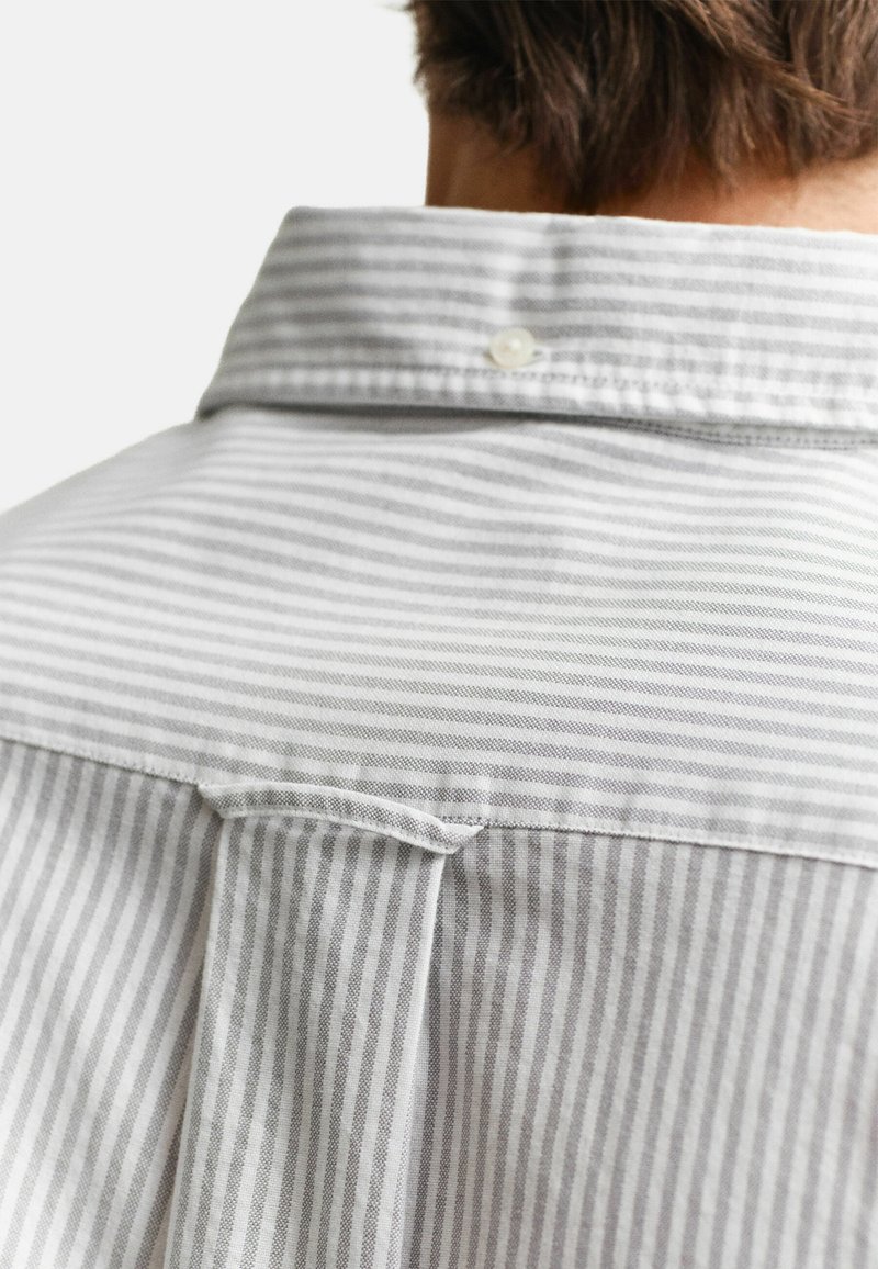 Rückenansicht einer Person, die ein weißes und grau vertikal gestreiftes Hemd mit Knopfleiste und geknöpftem Kragen trägt.