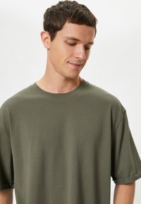 Olivenfarvet bomulds t-shirt med afslappet pasform, korte ærmer og rund halsudskæring, prydet med et tekstureret stof og minimal dekoration.