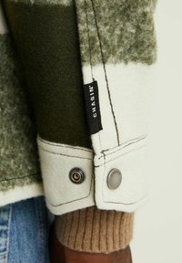 Fleecejack met groene en witte tonale blokken, voorzien van een drukknoopsluiting, ribbelige bruine manchet en een zwart merkteken.