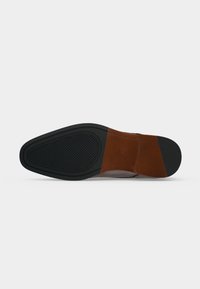 Chaussure habillée à semelle en cuir vue du dessous, avec des protections en caoutchouc noir texturé au niveau des orteils et du talon et une section centrale lisse marron.