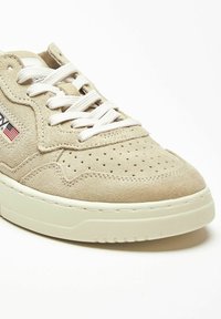 Sneakers in camoscio beige con punta traforata, lacci bianchi e suola in gomma color crema. Presentano un piccolo dettaglio con la bandiera americana sul lato.