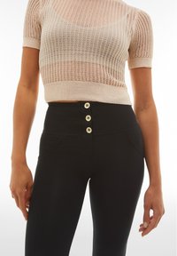 Pantalones negros de tiro alto con cuatro botones frontales, de diseño elegante y con bolsillos laterales. Top de punto acanalado semi-translúcido en color beige claro con mangas cortas.