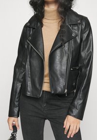 Veste de moto noire en simili cuir avec un design court, fermeture éclair argentée, et poches latérales zippées ; dotée d'un col pointu et d'une finition texturée.