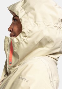 Beige wasserdichte Jacke mit hohem Kragen, durchgehendem Reißverschluss und Kapuze. Merkmale ein kontrastierendes Innenfutter in Orange und gesticktes Logo der Marke.