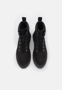 Botas de tobillo negras en material mate con un cuello acolchado, punta redonda y cordones grises. Presentan ojales metálicos y una suela de goma gruesa.