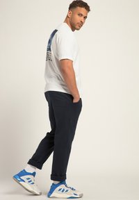 Witte t-shirt met blauwe grafische print op de rug, marineblauwe broek en blauw-witte sneakers. Katoenen stof, losse fit, opgerolde broekspijpen.