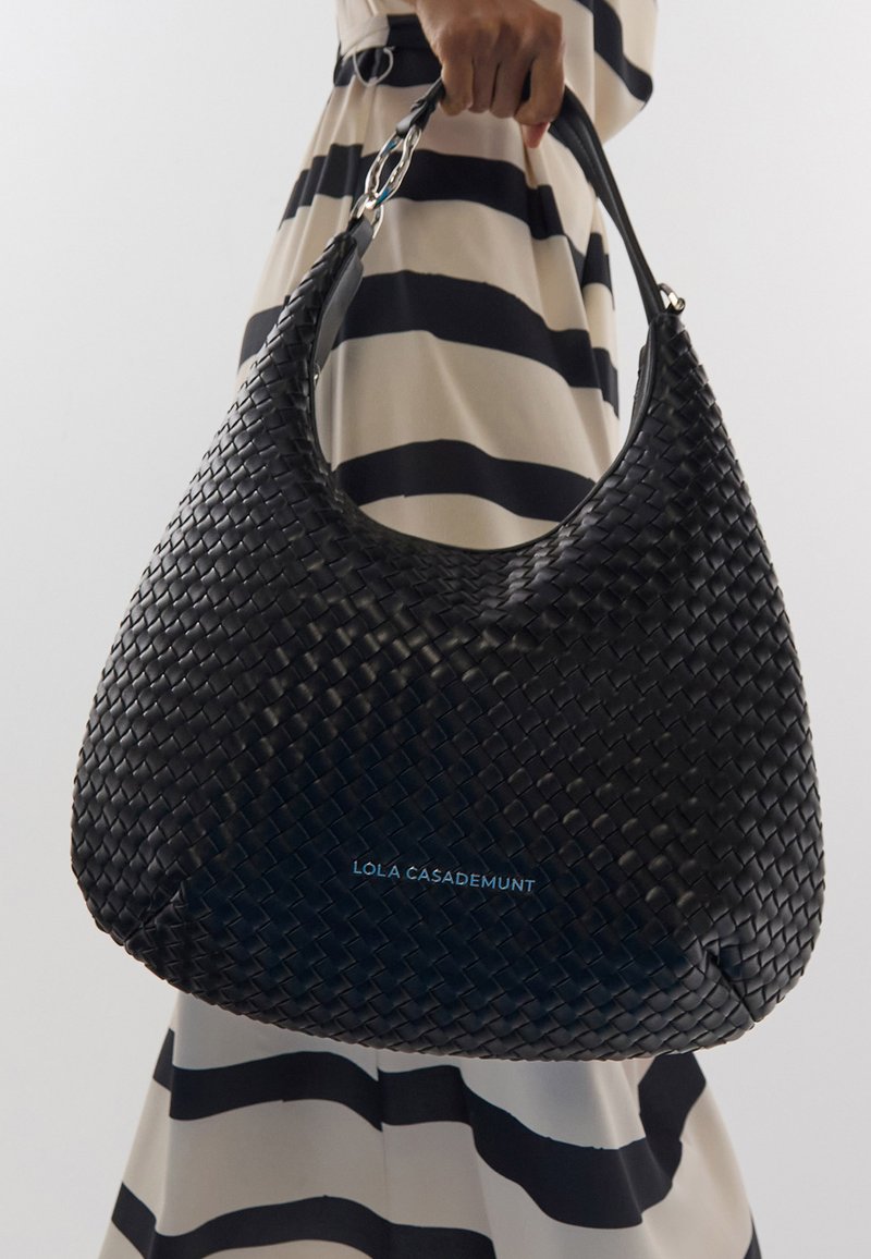 Sac hobo tissé noir avec une texture lisse et une large anse. Présente un logo en bleu clair. Le sac a une forme arrondie.