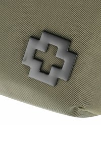 Borsa in tessuto verde scuro caratterizzata da un emblema a croce nera in rilievo. Superficie testurizzata con dettagli di cucitura visibili. Forma compatta e rettangolare.