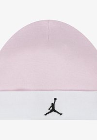 Lyserød ribstrikket hue med en hvid kant. Har et sort Jordan-logo foran. Blød tekstur med en tætsiddende pasform.
