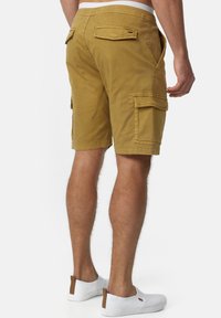 Brune cargo-shorts med sidelommer og baglommer, stikninger og en afslappet pasform. Båret med hvide slip-on sko.