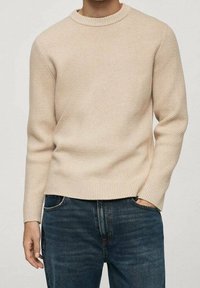 Pull beige en maille avec un col rond, un motif texturé et des poignets et un ourlet côtelés. Associé à un jean en denim bleu foncé.