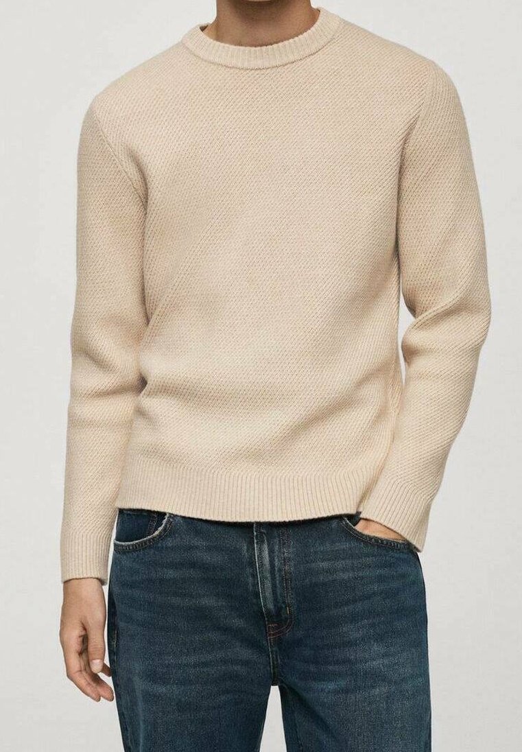 Pull beige en maille avec un col rond, un motif texturé et des poignets et un ourlet côtelés. Associé à un jean en denim bleu foncé.