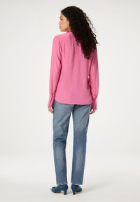 Lange mouw roze blouse met geplooid detail aan de achterkant, gecombineerd met lichtblauwe spijkerbroek en blauwe hoge hakken.