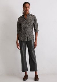 Black button-up shirt with a floral pattern, paired with gray leather wide-leg pants. Model stands on a neutral background.
