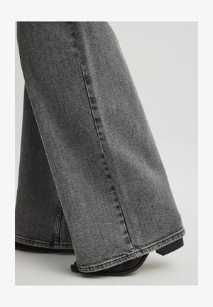 Platas kājas džinsi tumši pelēkā džinsā, ar gludu tekstūru, redzamām šuvēm un tīru maliņu. Apvienoti ar melniem papēžu sandālītēm.