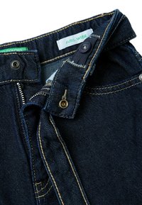 Tmavě modré džíny z denimu s širokým pasem, žlutým šitím, předním zipem a zapínáním na knoflík. Štítek nese nápis "AVRIL-WIDE".