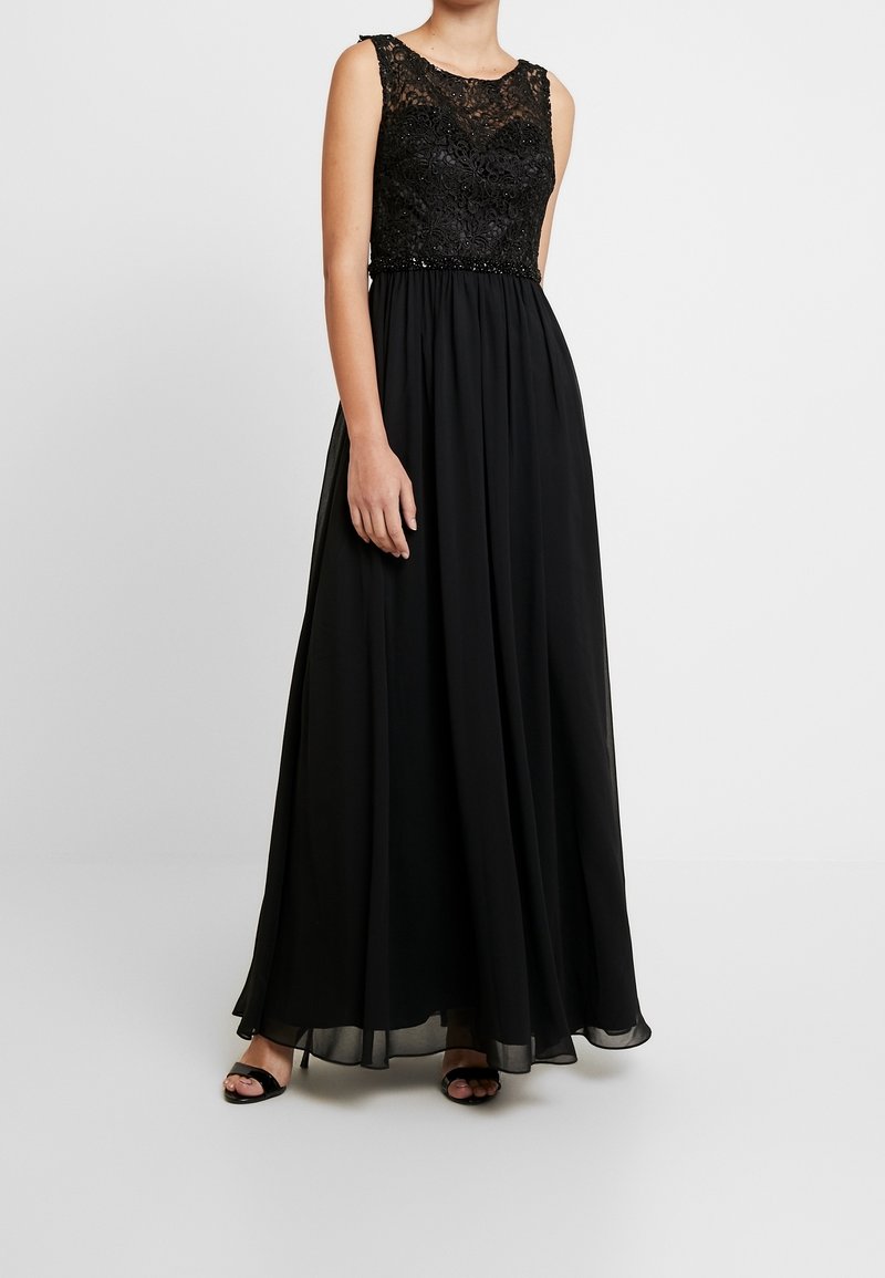 Svart klänning med en spetsliv och pärlbesatt midja. Flödar ut i en plisserad kjol. Ärmlös design med rund halsringning. Slät tygtextur.