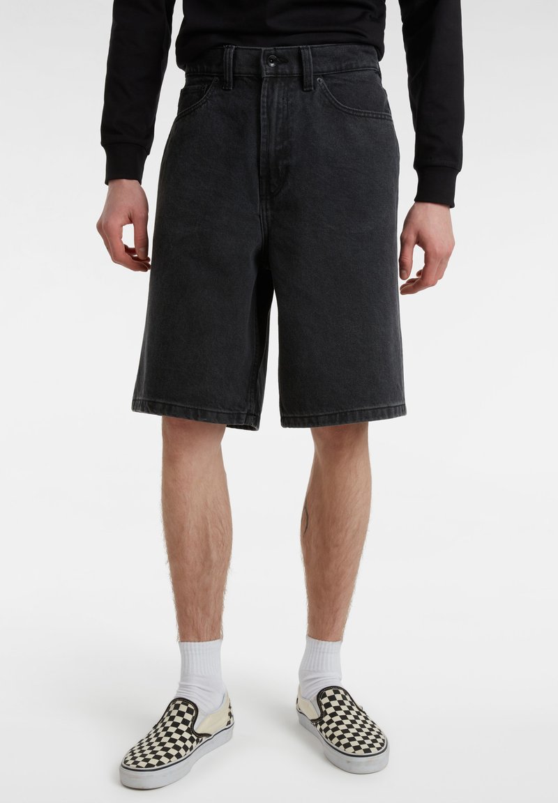 Shorts in denim nero con una vestibilità rilassata, passanti per cintura e taglio dritto, abbinati a scarpe slip-on a quadretti e calzini bianchi alla caviglia.