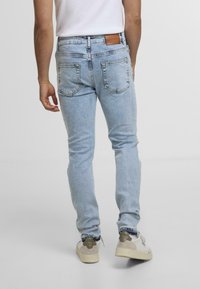 Heledad sinine teksapükste slim fit lõige, millel on tagataskud ja nahast detaile vöökoht. Stiliseeritud valgete tossudega.