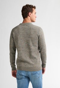 Maglione grigio e marrone a fantasia con scollo rotondo, maniche lunghe e polsini a coste, abbinato a jeans azzurri chiari.