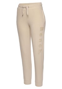 Beige Jogginghosen aus weichem Material mit elastischem Bund und Kordelzug, seitlichen Taschen und dezentem "Bench."-Druck.