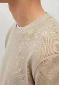 Sweatshirt en maille beige avec un tissu texturé, encolure ronde et légère finition côtelée aux poignets et à l'ourlet. Coupe standard et style col rond.