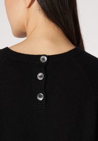 Schwarzer Strickpullover mit Rippkragen, der entlang des hinteren Halsausschnitts mit drei metallischen Knöpfen für den Verschluss und zur Dekoration versehen ist.