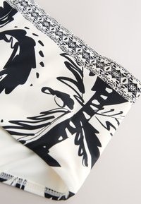 Crno-bijela tkanina s detaljnim cvjetnim i geometrijskim uzorcima duž ruba, prikazuje krupni plan teksture i dizajna tkanine.