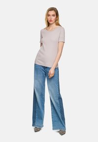 Hellgraues Kurzarmoberteil kombiniert mit weit geschnittenen blauen Jeans. Die Jeans haben ein zweifarbige Design, und das Outfit wird durch spitze Schuhe mit Leopardenmuster ergänzt.