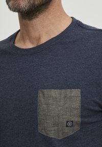 T-maica mornarice z modrim patč pocetkom s majhnim logotipom. Tkanina se zdi mehka z rahlo teksturo in okroglim izrezom.