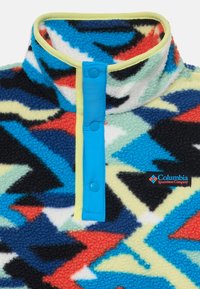 Pullover en polaire avec col haut, motif géométrique coloré en bleu, rouge et noir. Dispose d'une bordure jaune et de boutons-pression bleus. Logo présent.