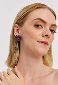 Lillelille kõrvarõngad, millel on roosa ja musta aktsendi kombinatsioon ning rippuvad rohelised lehed, valmistatud metallist ja kaunistatud gemstone'idega.