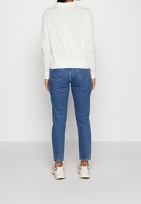 Light beige pullover with a round neckline, paired with fitted blue denim jeans. The outfit is completed with light-colored sneakers.