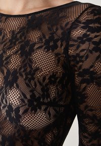 Schwarzes Spitzenoberteil mit floralen Mustern, die eine transparente Textur und eine taillierte Passform aufweisen, und sowohl Netz- als auch feste florale Details zeigen.