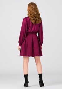 Lyhythihainen, luumunvärinen mekko, jossa on kaitaleet ja solmittava vyötärö. Sileä kangas, pyöreä pääntie ja yhdistetty mustien nilkkasaappaiden kanssa.