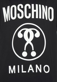 Tela negra con texto en negrita blanco "MOSCHINO" encima de un logo circular y texto "MILANO" debajo.