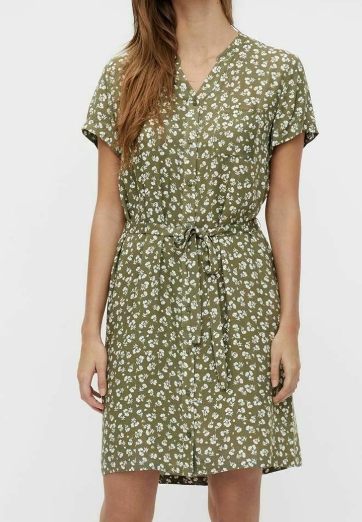 Femme portant une robe olive à manches courtes avec imprimé floral blanc, boutonnée sur le devant et ceinture nouée à la taille.