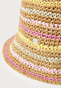 Un chapeau en paille à large bord présente un motif tissé avec des rayures pastel roses, jaunes et bleues. Comprend un accent métallique rond.