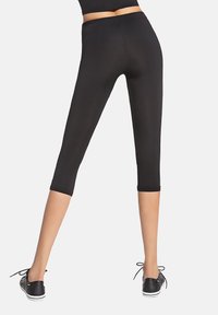 Czarne, dopasowane legginsy capri o gładkiej fakturze. Posiadają szeroki pas i skróconą długość, zestawione z czarnymi niskimi trampkami.