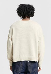 Cream knit sweater with relaxed fit, ribbed cuffs and hem, and a rounded neckline. Features a textured fabric pattern.