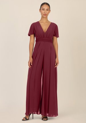 V-neck burgundy jumpsuit with short flutter sleeves, pleated design, fitted waist, and wide leg openings. Made from lightweight fabric.