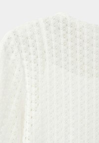 Tissu en dentelle blanche avec un motif floral délicat et complexe formant une surface texturée semi-transparente.