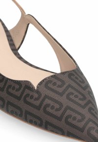 Chaussure plate à bout pointu en tissu marron foncé avec un motif géométrique noir répétitif. Présente un design ajouré et une semelle intérieure beige.