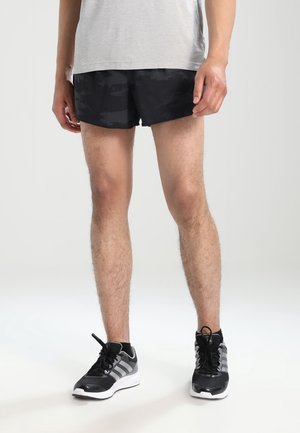 Zwarte camouflage sportieve korte broek met een getextureerd oppervlak, gecombineerd met zwarte en grijze hardloopschoenen met veters en een witte zool.