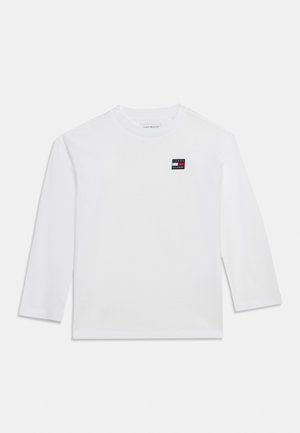 T-shirt blanc à manches longues Tommy Hilfiger avec un petit écusson logo sur la poitrine, présenté sur un fond uni.