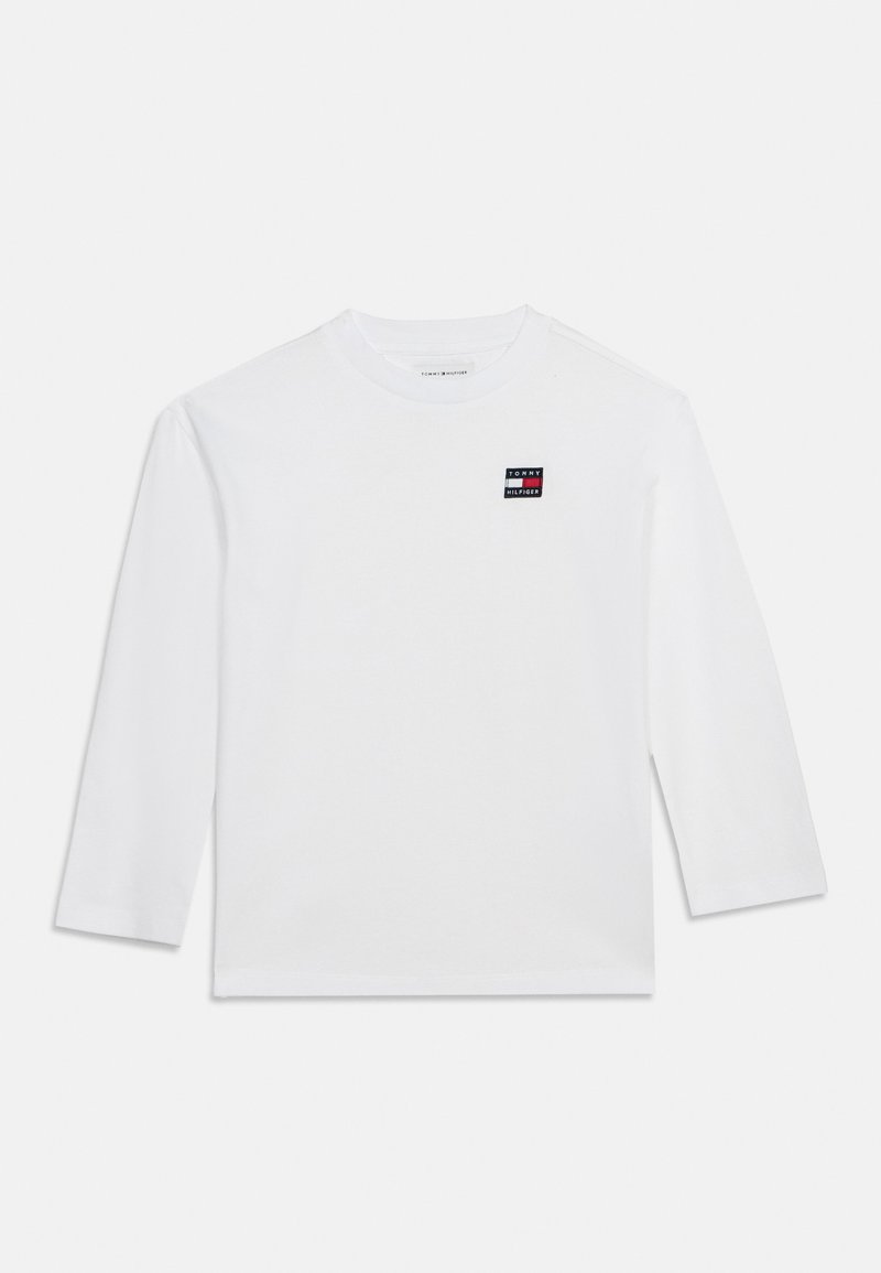 T-shirt blanc à manches longues Tommy Hilfiger avec un petit écusson logo sur la poitrine, présenté sur un fond uni.